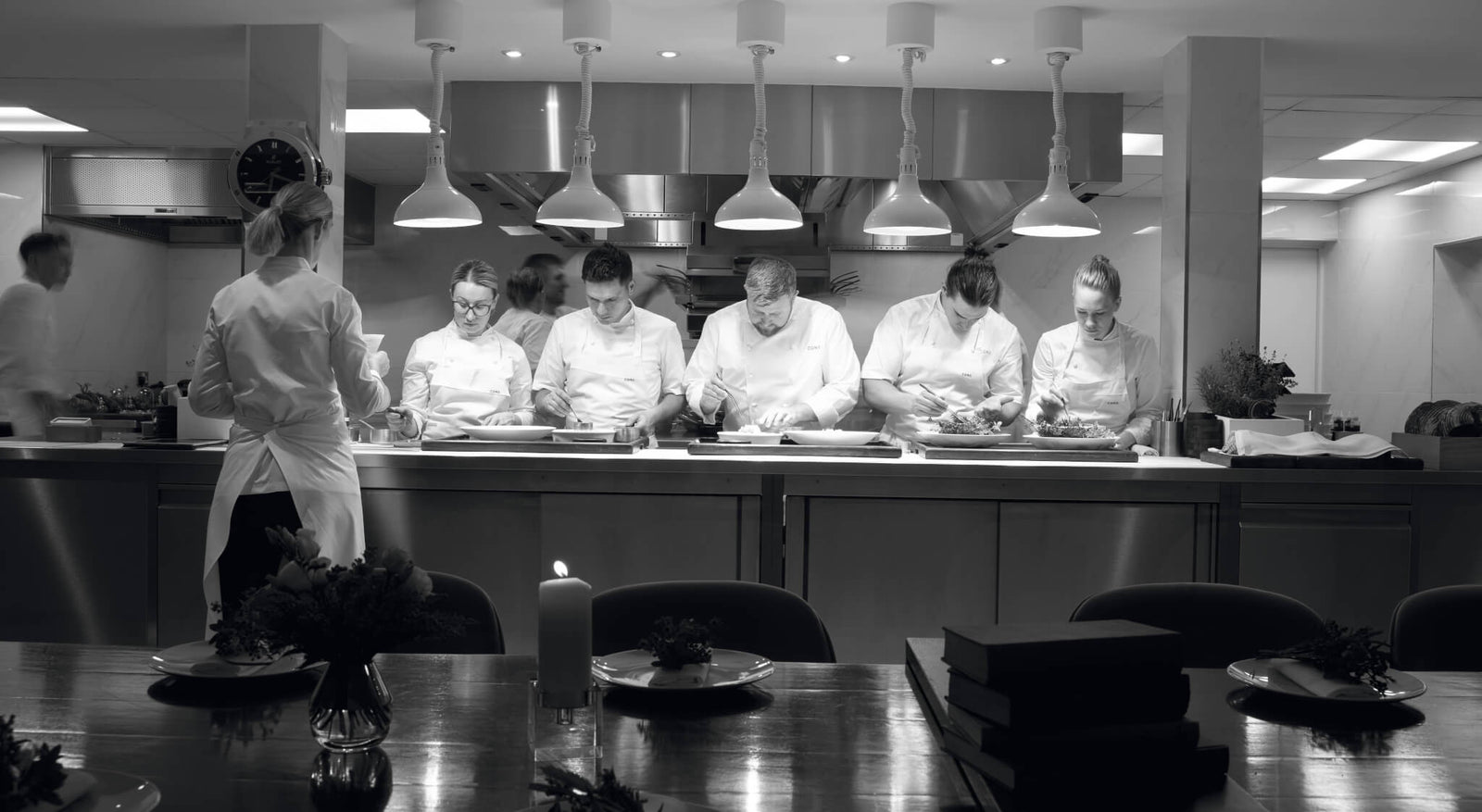 chefs working in a modern kitchen preparing gourmet dishes in a professional setting with a dining table in the foreground