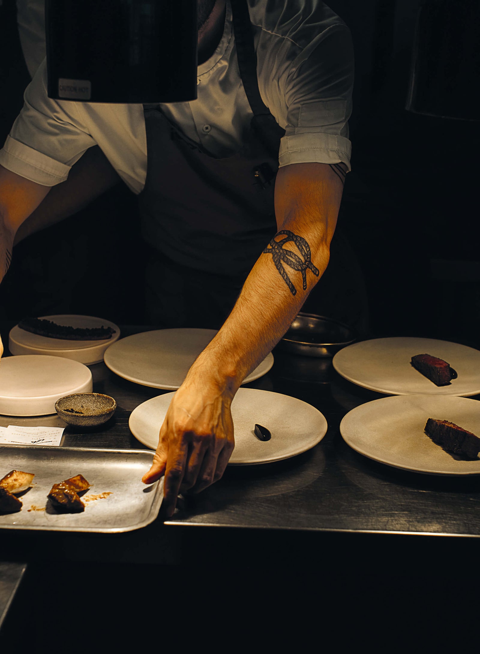 chef plating gourmet dishes in a dimly lit restaurant kitchen with elegant ceramic plates and artistic food presentation