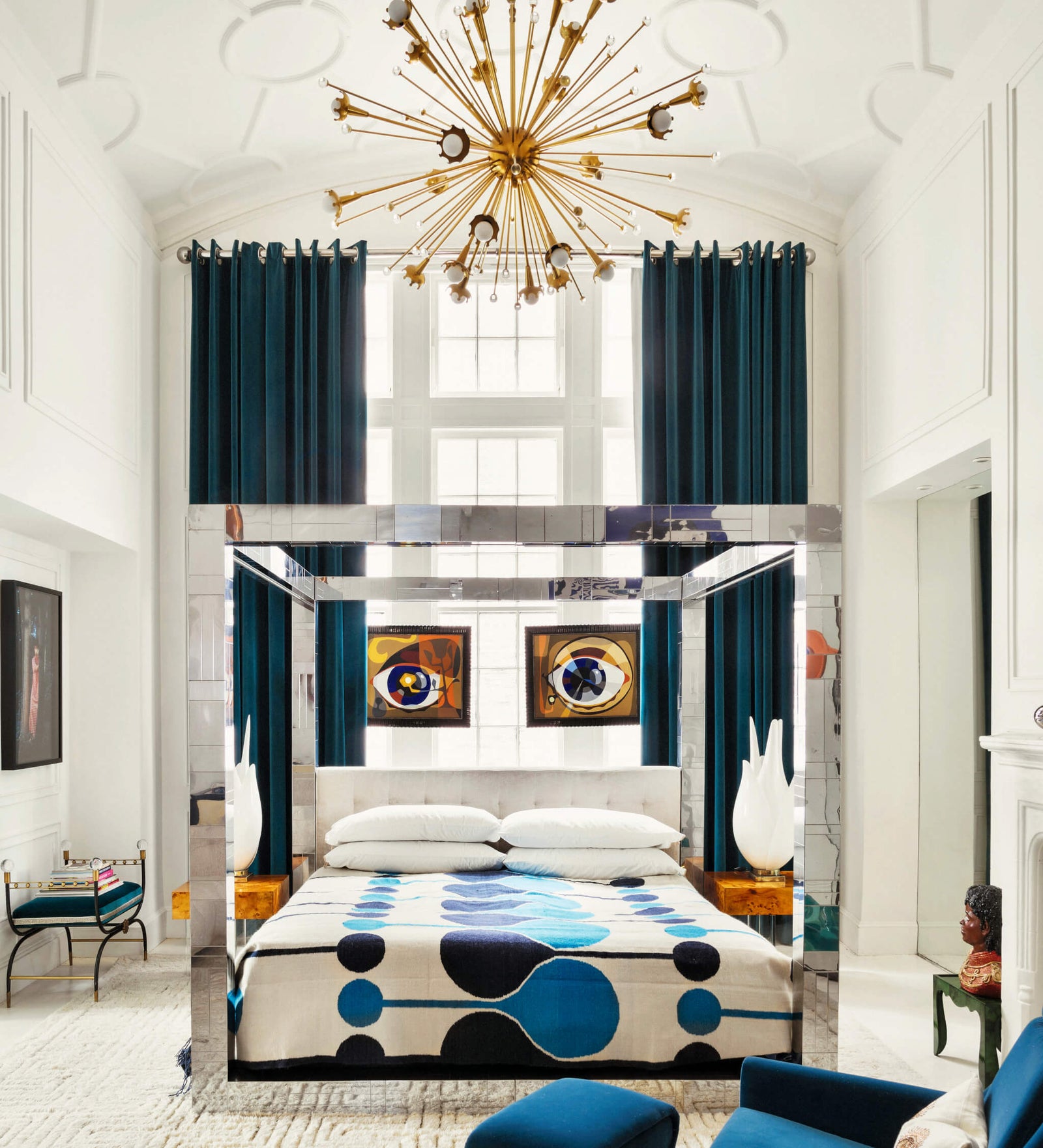 modern bedroom design with a four-poster mirror bed, blue and white patterned bedding, vibrant blue curtains, starburst chandelier, abstract artwork, and stylish furnishings