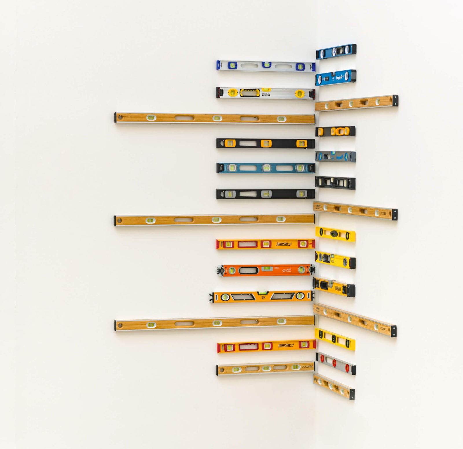 collection of various spirit levels arranged on a corner wall, featuring different colors and designs