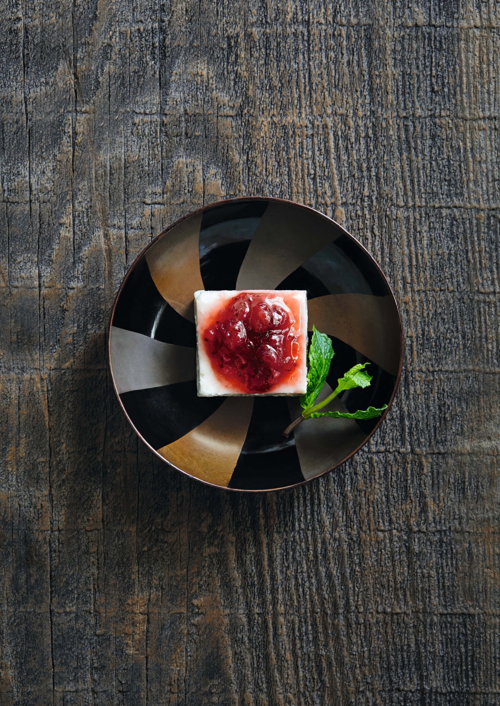 dessert on a decorative plate with berry sauce and mint leaf on rustic wooden background