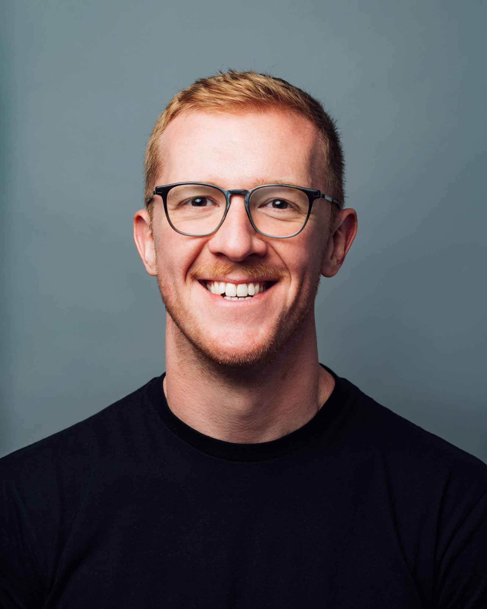 Smiling young man with glasses wearing a black t-shirt against a gray background