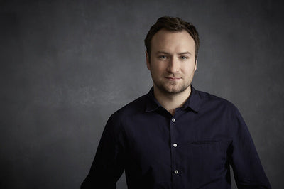 portrait of david gelb smiling wearing a black shirt against a neutral background