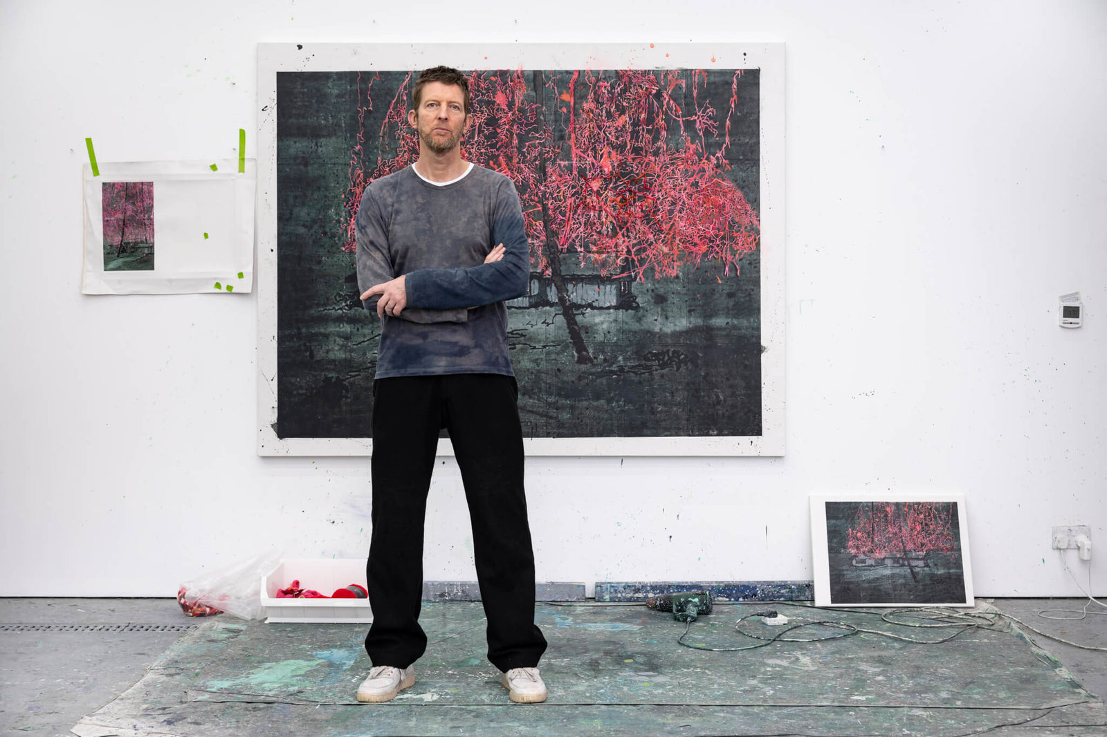 artist standing in studio with vibrant artwork and sketches on walls, surrounded by paint splatters and art supplies