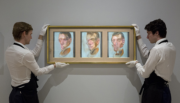 Two Sotheby's employees with Francis Bacon, Three Studies for Self-Portrait, 1980, oil on canvas, each: 35.5 by 30.5cm est. £10-15 million. Image courtesy of Sotheby’s