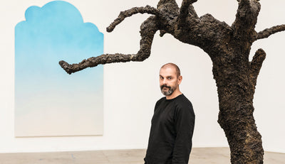 man standing next to abstract art and a sculpture of a tree with a blue and white background in an art gallery