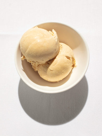 scoops of creamy beige ice cream in a white bowl on a light background