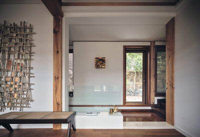 interior design of a modern living space featuring wooden beams, a unique wall art piece, a glass barrier, and a stylish coffee table with decorative items and a window overlooking outdoor greenery