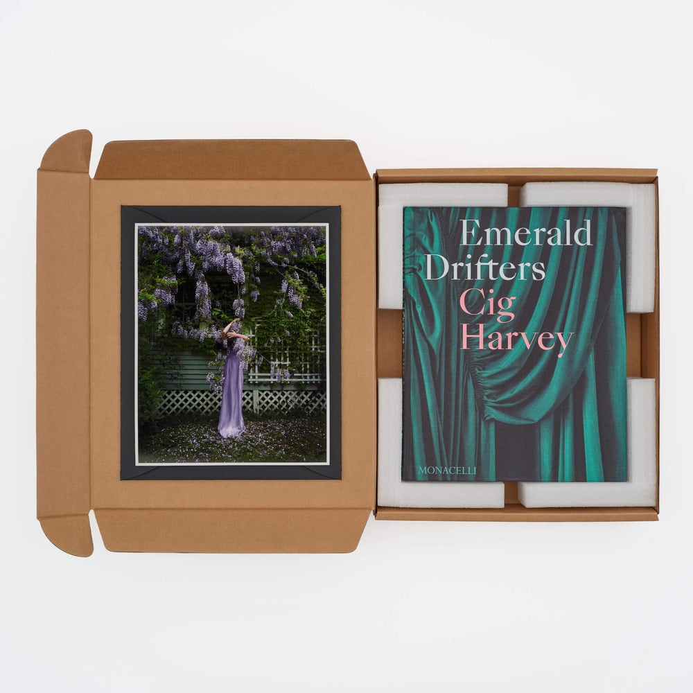 Photograph of a woman in a lavender gown under blooming wisteria, accompanied by the book "Emerald Drifters" by Cig Harvey in a cardboard box packaging.