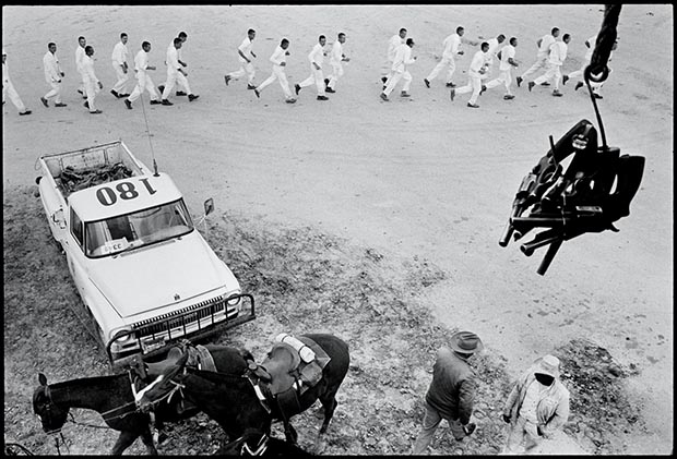 Guns are passed to the picket tower; the line returns from work. Ferguson. From Conversations with the Dead 