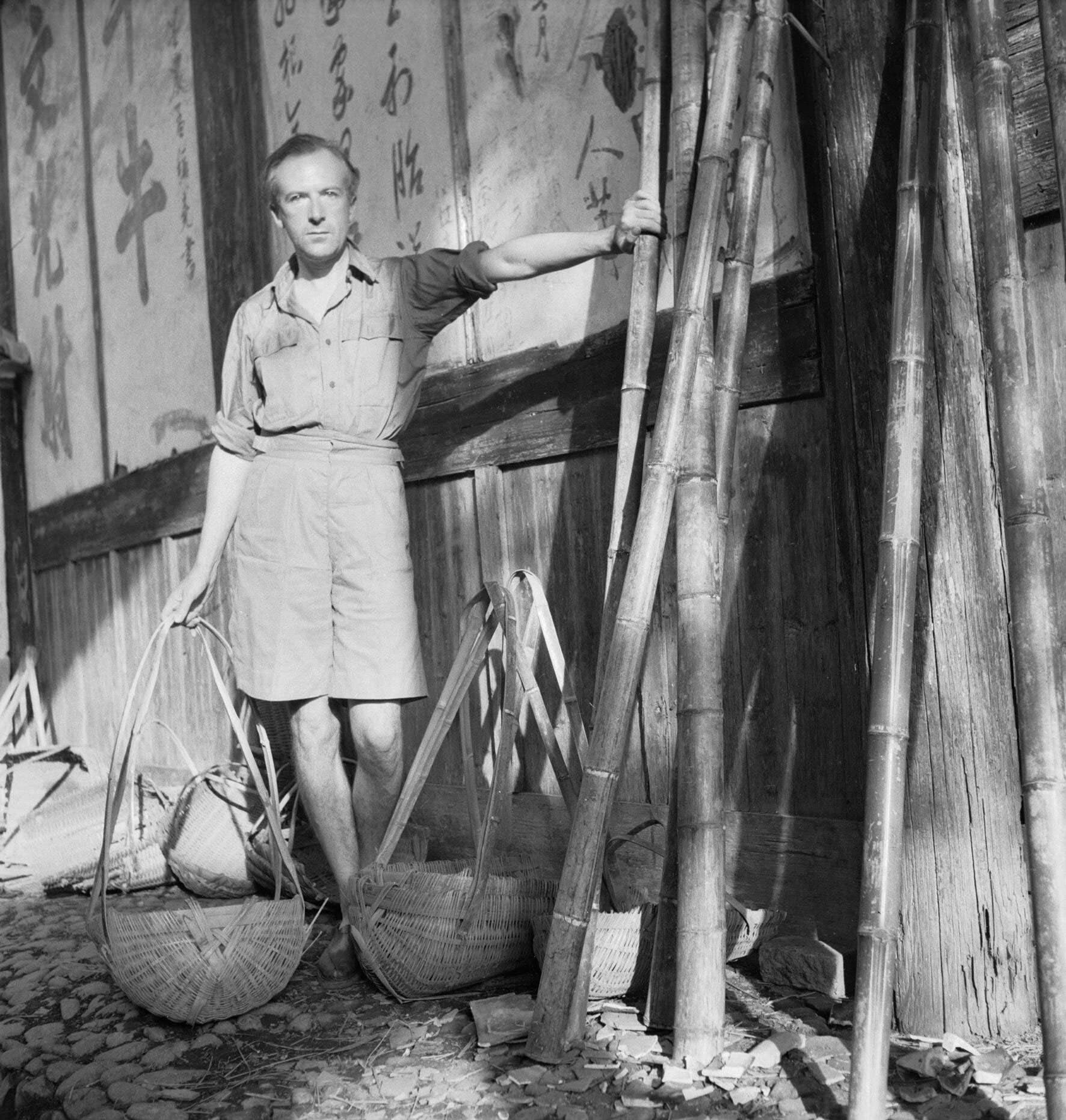 Cecil Beaton with wicker baskets beside a wall with Chinese characters in Puncheng in south eastern China, during World War II. Image courtesy of the Ministry of Information, via Wikimedia Commons
