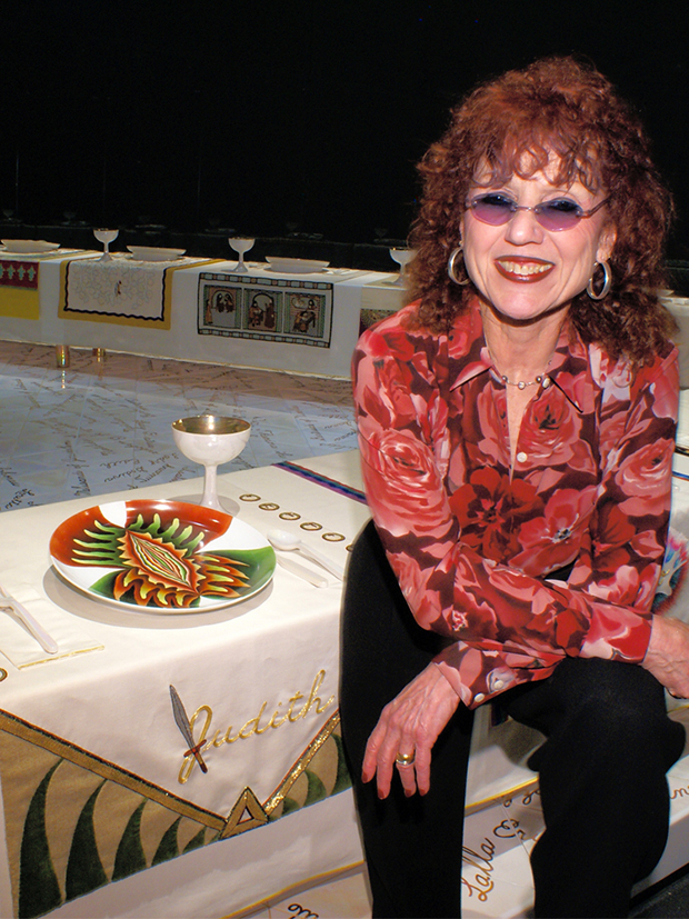 Judy Chicago beside the place setting for Judith, the Old Testament figure Judith. Image courtesy of Judy Chicago.